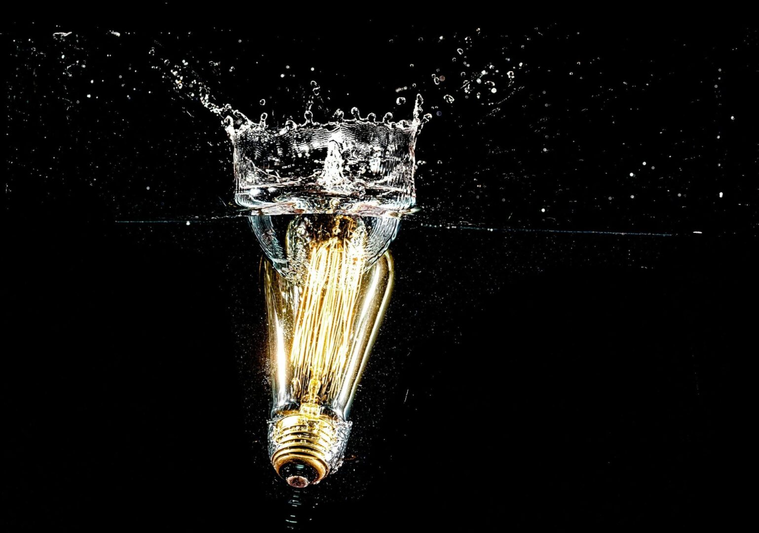 A light bulb is submerged in water with the reflection of it.